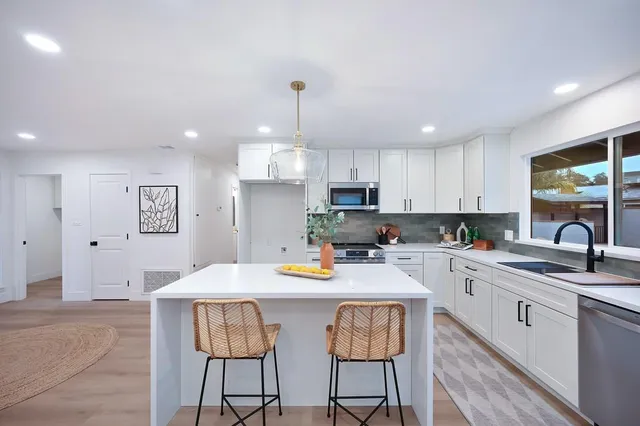 a kitchen with stainless steel appliances kitchen island granite countertop a stove a sink a refrigerator and white cabinets with wooden floor