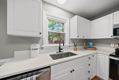 a kitchen that has a lot of white cabinets a sink a window and stainless steel appliances