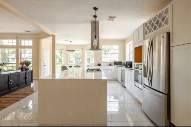 a kitchen with stainless steel appliances granite countertop a refrigerator a sink dishwasher a stove and a dining table with wooden cabinet