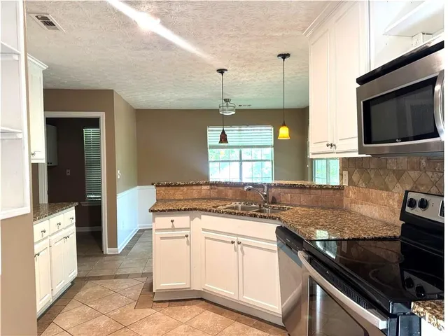 a kitchen with stainless steel appliances granite countertop a refrigerator a sink and white cabinets