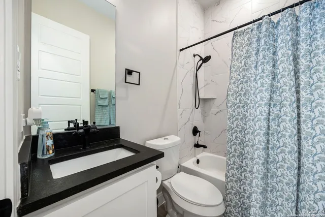 a bathroom with a granite countertop sink a toilet and shower curtain