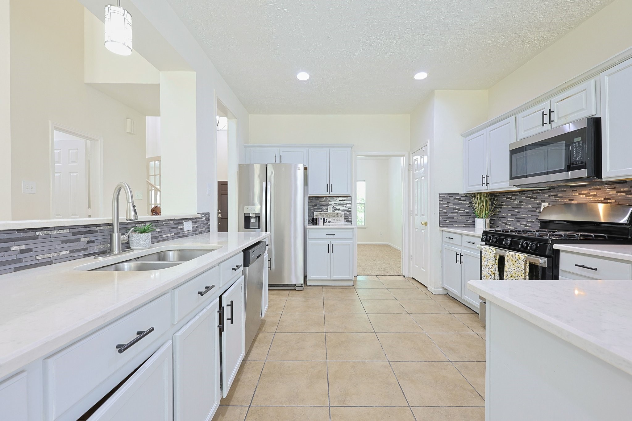 23019 Eastgate Village Drive Spring, TX 77373 - Photo 10 of 46 Bright and modern kitchen with ample counter space, stainless steel appliances, and stylish tile backsplash. Features white cabinetry, recessed lighting, and a double sink, providing a clean and functional cooking area.