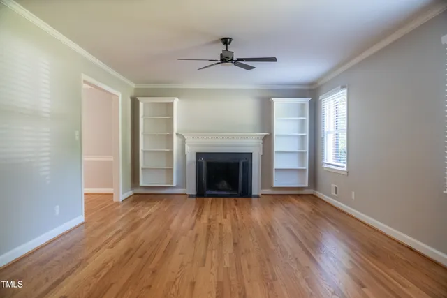 a view of an empty room with wooden floor fireplace and a window