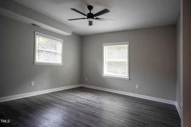 a view of an empty room with wooden floor and a ceiling fan