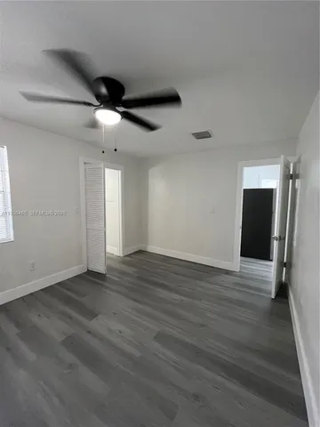 a view of an empty room with wooden floor and a ceiling fan