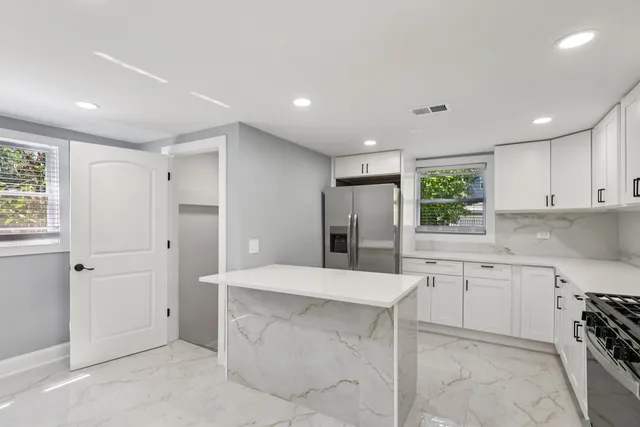 a large white kitchen with stainless steel appliances kitchen island granite countertop a refrigerator a sink a stove and white cabinets with wooden floor