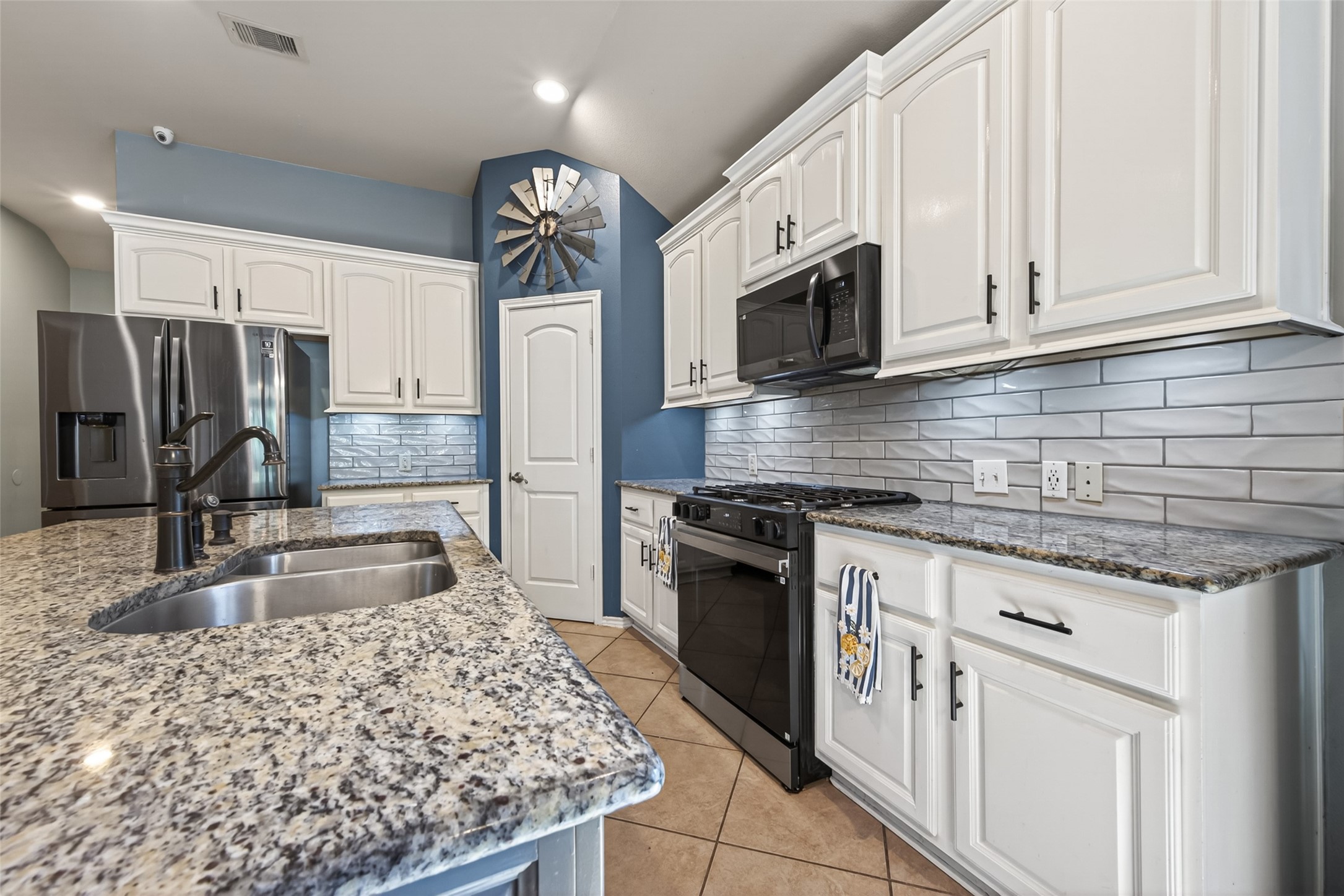 27443 Rebecca Field Lane Spring, TX 77386 - Photo 11 of 31 This kitchen features granite countertops, a central island with a sink, and sleek stainless steel appliances. The white cabinetry complements the subway tile backsplash, creating a modern and inviting space.