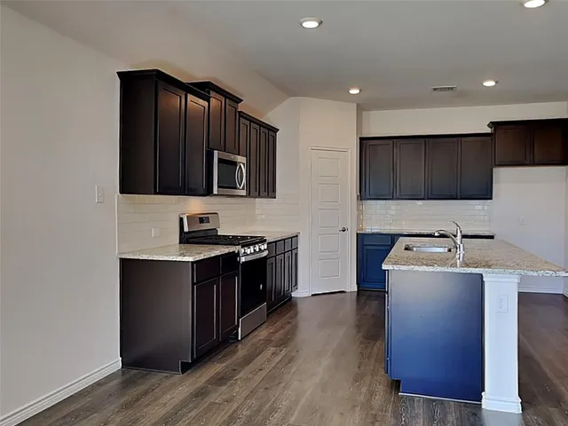 a kitchen with stainless steel appliances granite countertop a stove top oven a sink dishwasher and a refrigerator with wooden floor