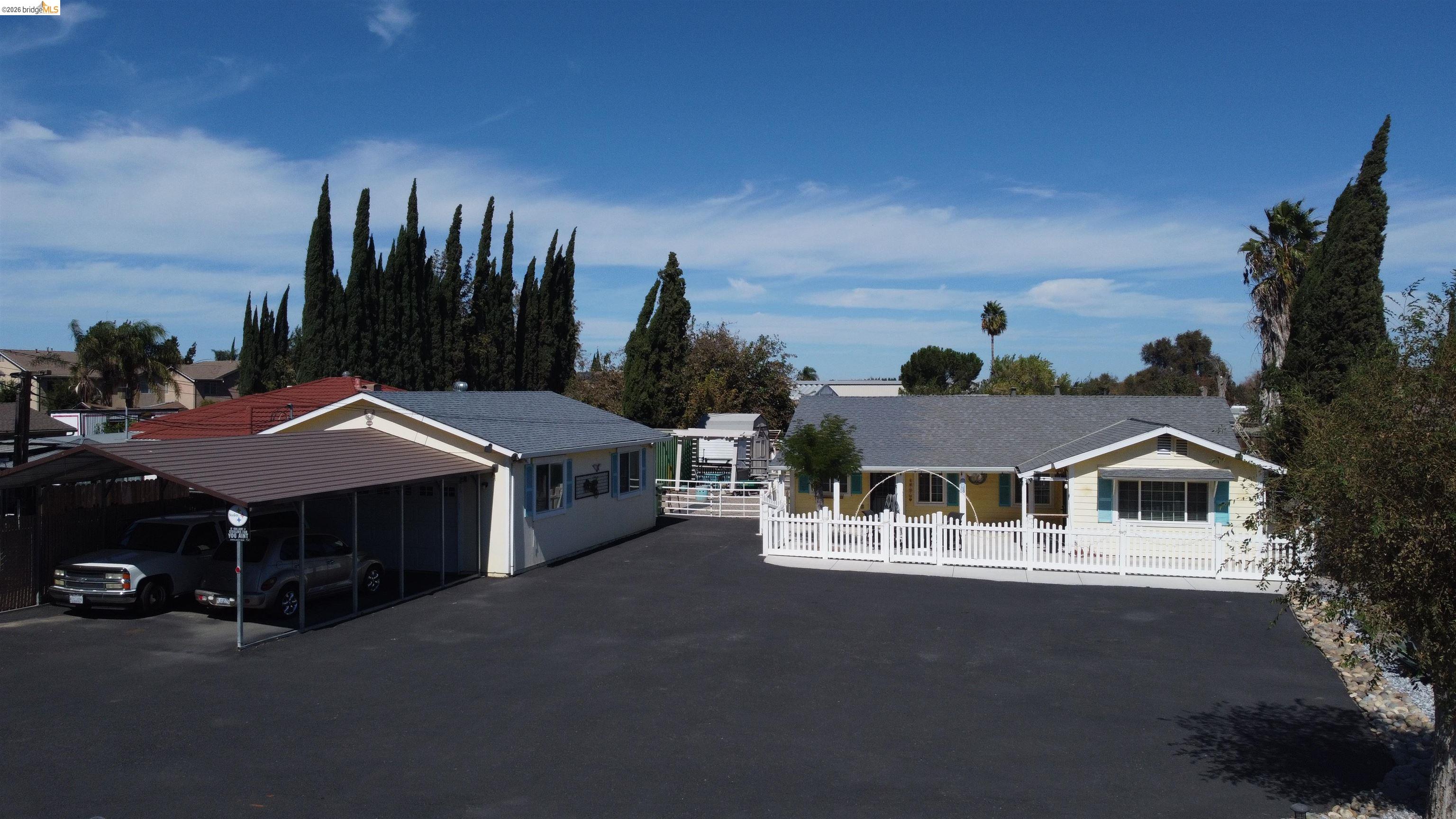 2831 Fabian Road Tracy, CA 95377 - Photo 1 of 23 Expansive paved driveway, attached carport, white picket fence, and mature trees framing the property