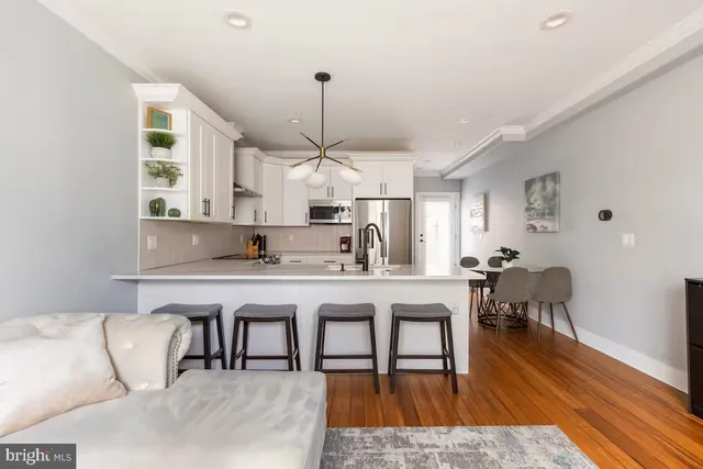 a living room with kitchen island furniture a wooden floor and a chandelier
