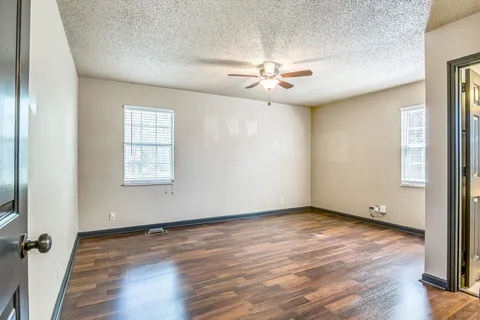 an empty room with wooden floor fan and windows