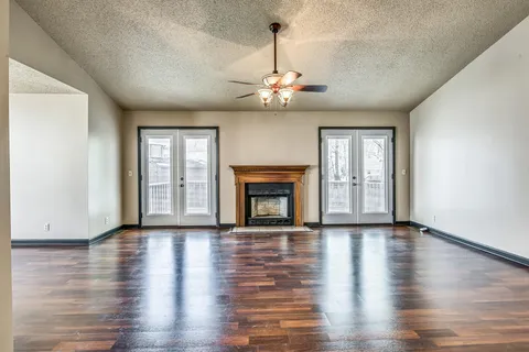 a view of an empty room with wooden floor fireplace and a window