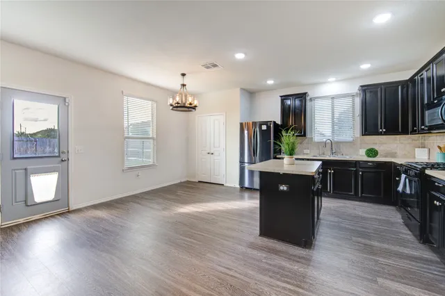 a kitchen with stainless steel appliances granite countertop a refrigerator a sink dishwasher a stove and a dining table with wooden floor