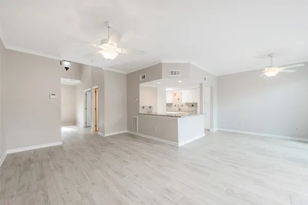 a view of an empty room and kitchen view with wooden floor