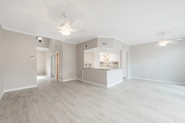 a view of an empty room and kitchen view with wooden floor