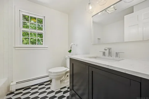 a bathroom with a sink a toilet a window and a mirror