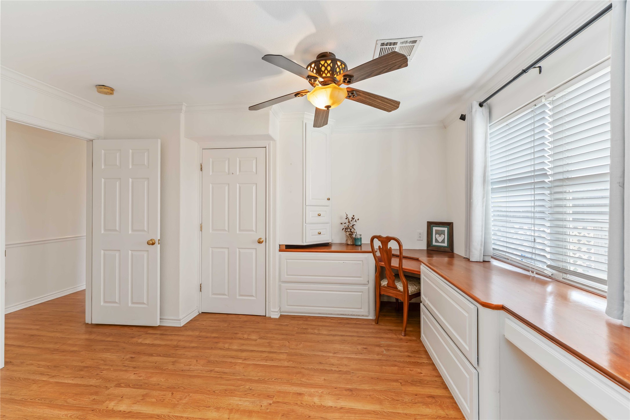 606 Packer Court Webster, TX 77598 - Photo 17 of 28 This bright, airy room features warm wood flooring, a ceiling fan, and abundant natural light from large windows with blinds.
It includes built-in cabinets and a desk, ideal for a home office or study space.