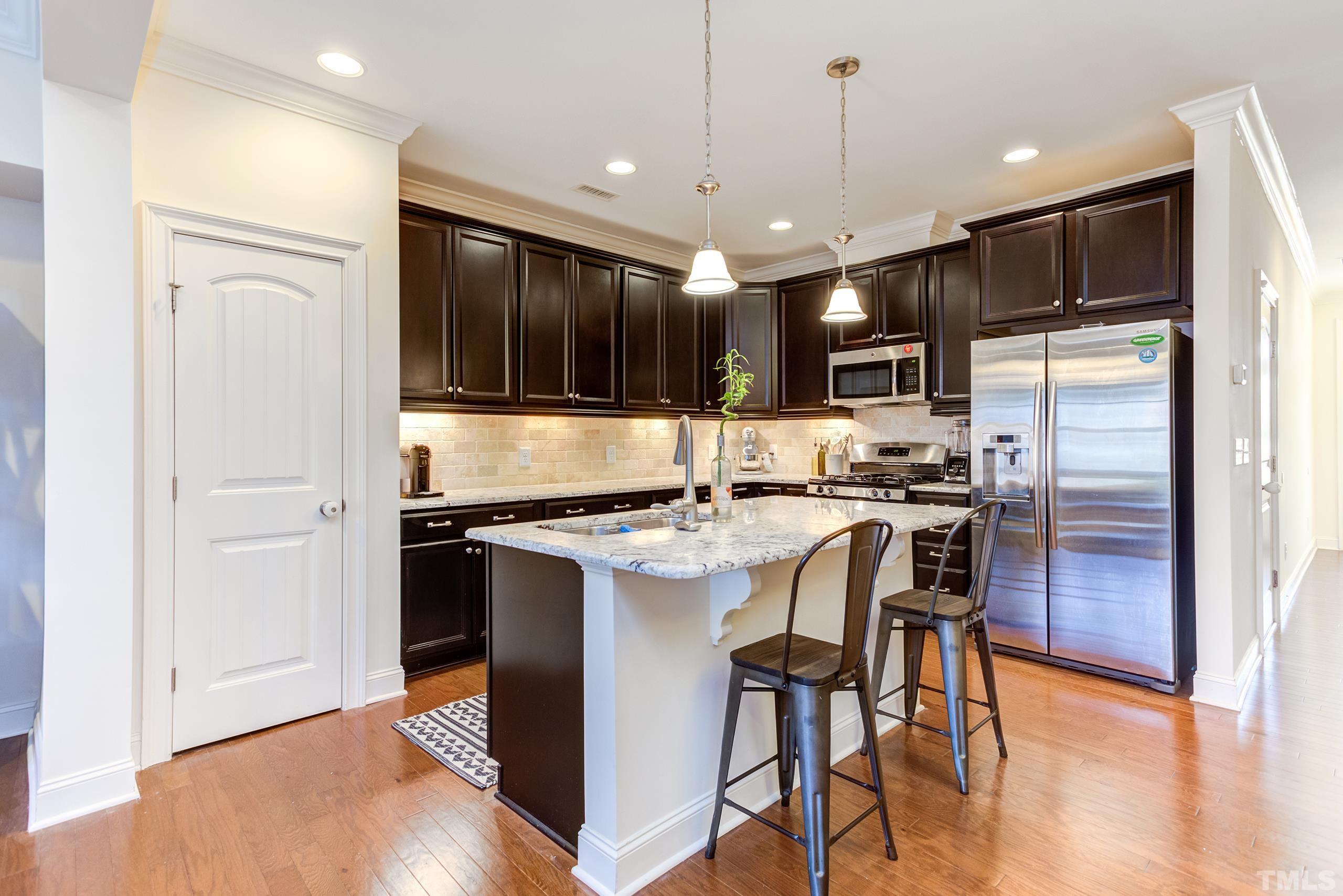 449 Talons Rest Way Cary, NC 27513 - Photo 11 of 54 a kitchen with stainless steel appliances granite countertop a stove top oven a refrigerator and a dining table with wooden floor