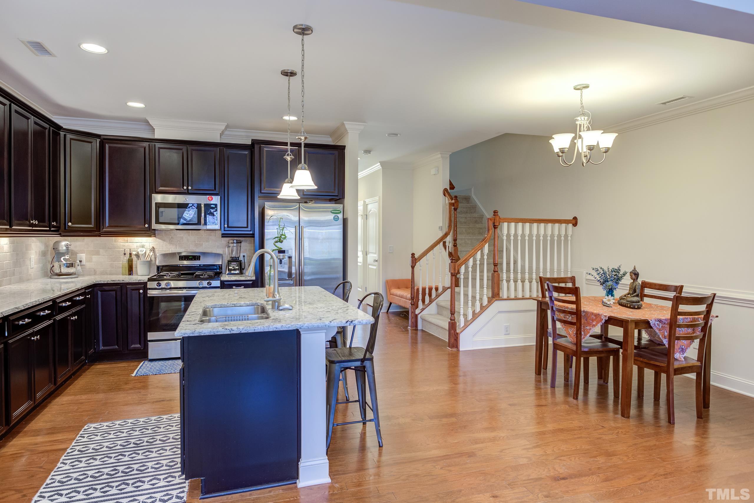449 Talons Rest Way Cary, NC 27513 - Photo 20 of 54 a kitchen with stainless steel appliances granite countertop a stove top oven a sink a dining table and chairs with wooden floor