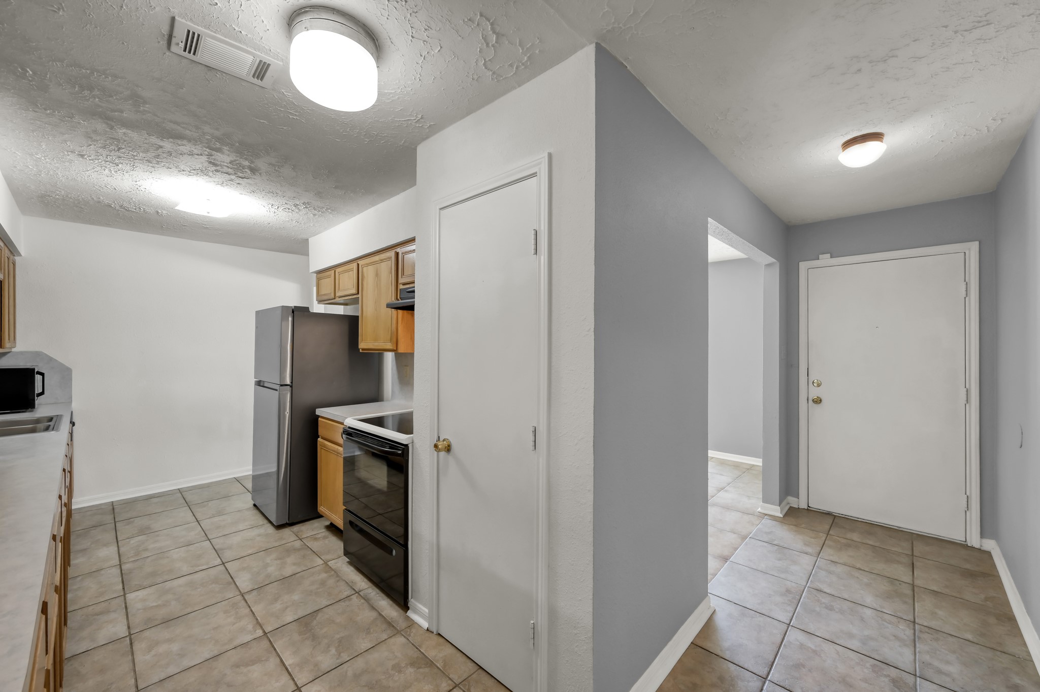 4314 Enchantedgate Drive Spring, TX 77373 - Photo 12 of 47 Tidy kitchen with tiled flooring, wooden cabinets, and modern appliances, leading into an adjacent entryway with a light gray color scheme and a white entry door.