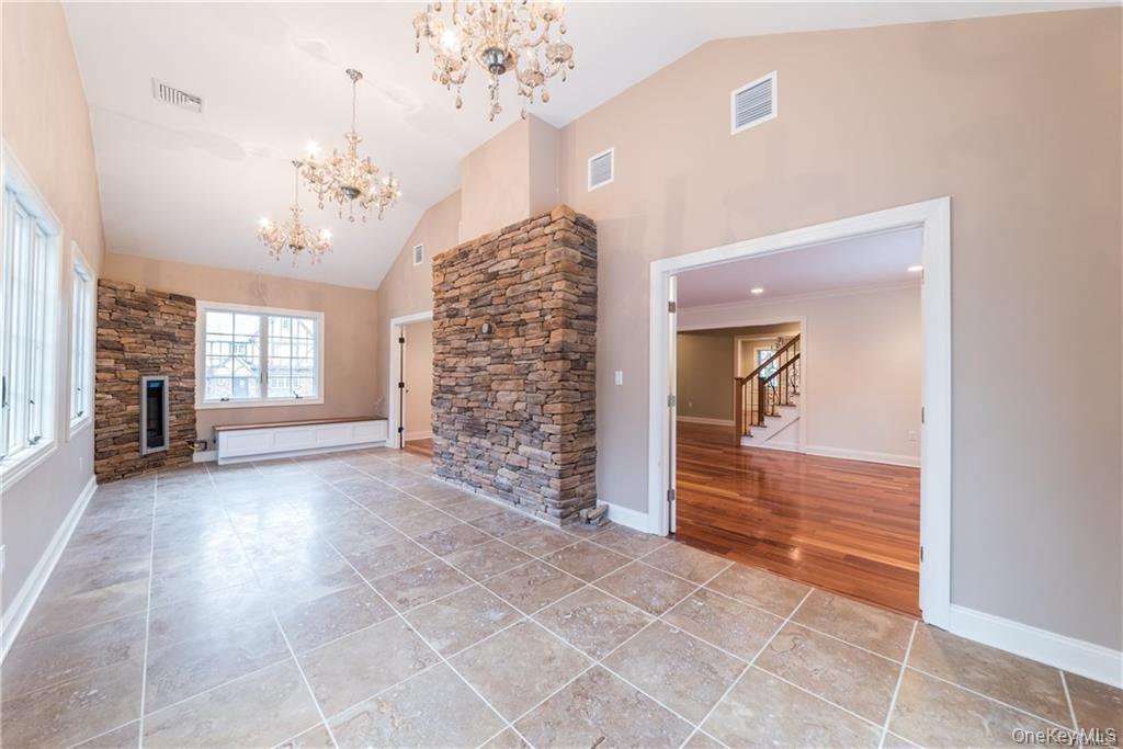 1 Elizabeth Road New Rochelle, NY 10804 - Photo 13 of 23 Unfurnished living room with a chandelier, high vaulted ceiling, stairway, a stone fireplace, and baseboards