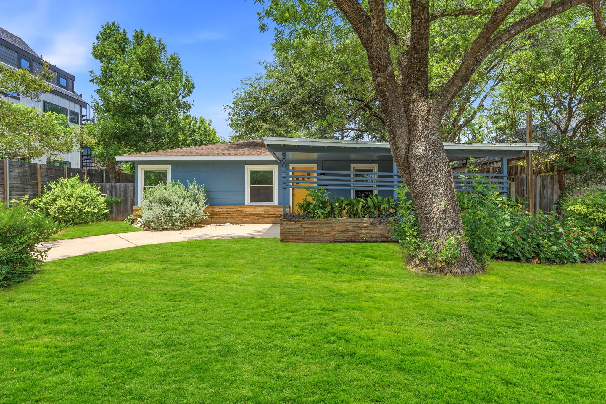 900 Stark Street Austin, TX 78756 - Photo 2 of 25 A charming blue home with a yellow front door and a well-kept lawn, nestled among mature trees.