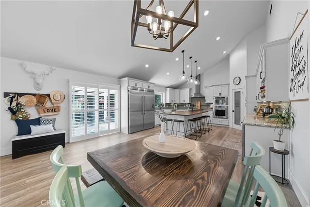 a kitchen with stainless steel appliances kitchen island granite countertop a refrigerator a stove a sink a dining table and chairs with wooden floor