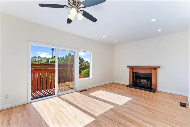 a view of an empty room with wooden floor fireplace and a window