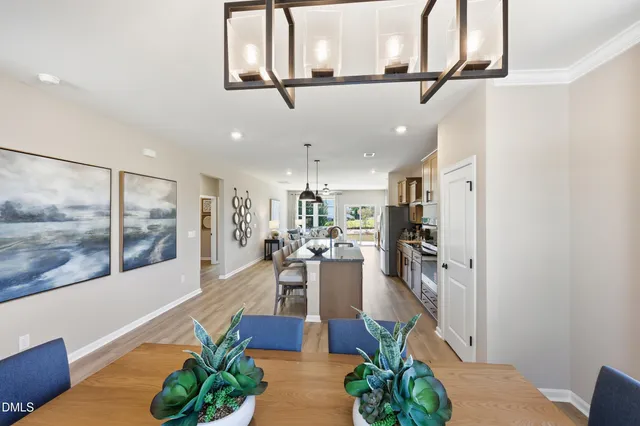 a kitchen with stainless steel appliances a refrigerator a sink dishwasher a dining table and chairs with wooden floor