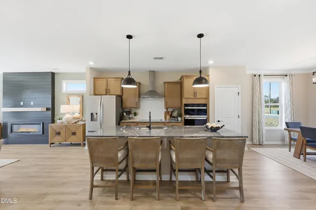 a kitchen with stainless steel appliances kitchen island granite countertop a stove a refrigerator a sink a dining table and chairs with wooden floor