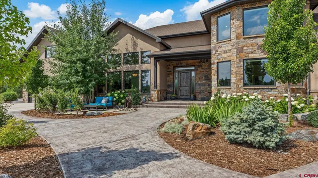 a view of a brick house with small yard plants and large tree