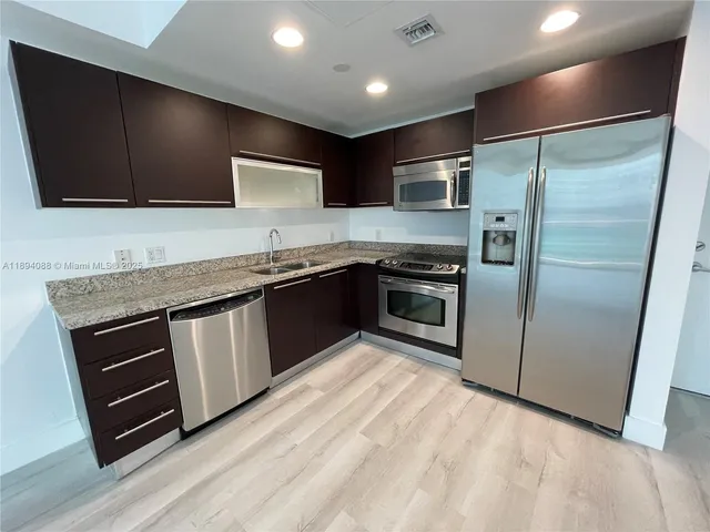 a kitchen with stainless steel appliances granite countertop a stove a sink and a refrigerator with wooden floor