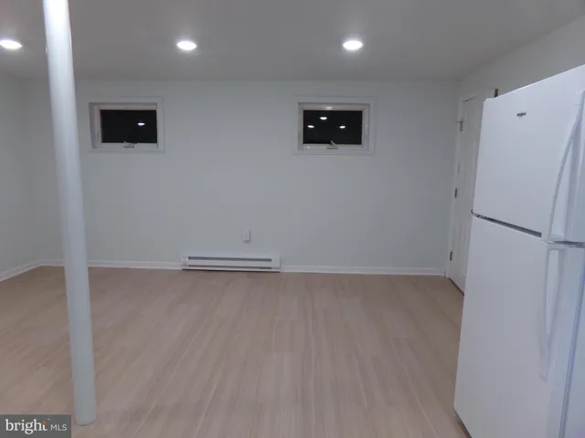 a view of a refrigerator in kitchen and an empty room with wooden floor