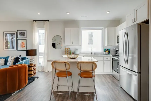 a kitchen with stainless steel appliances granite countertop a refrigerator a sink dishwasher a dining table and chairs with wooden floor
