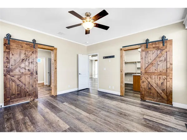 a view of an empty room with wooden floor and a ceiling fan