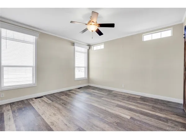 an empty room with wooden floor ceiling fan and windows