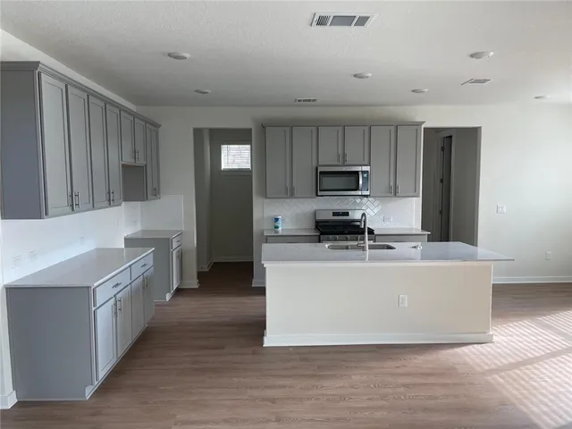 a living room with stainless steel appliances a kitchen island hardwood floor sink and a stove