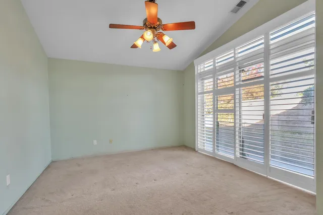 an empty room with chandelier fan and windows