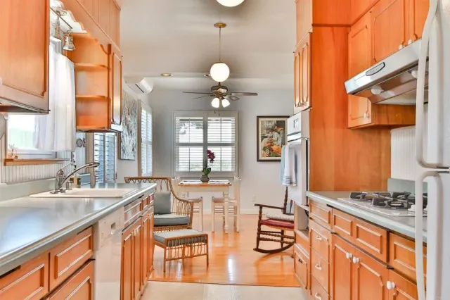 a kitchen with stainless steel appliances granite countertop a stove a sink dishwasher and white cabinets with wooden floor