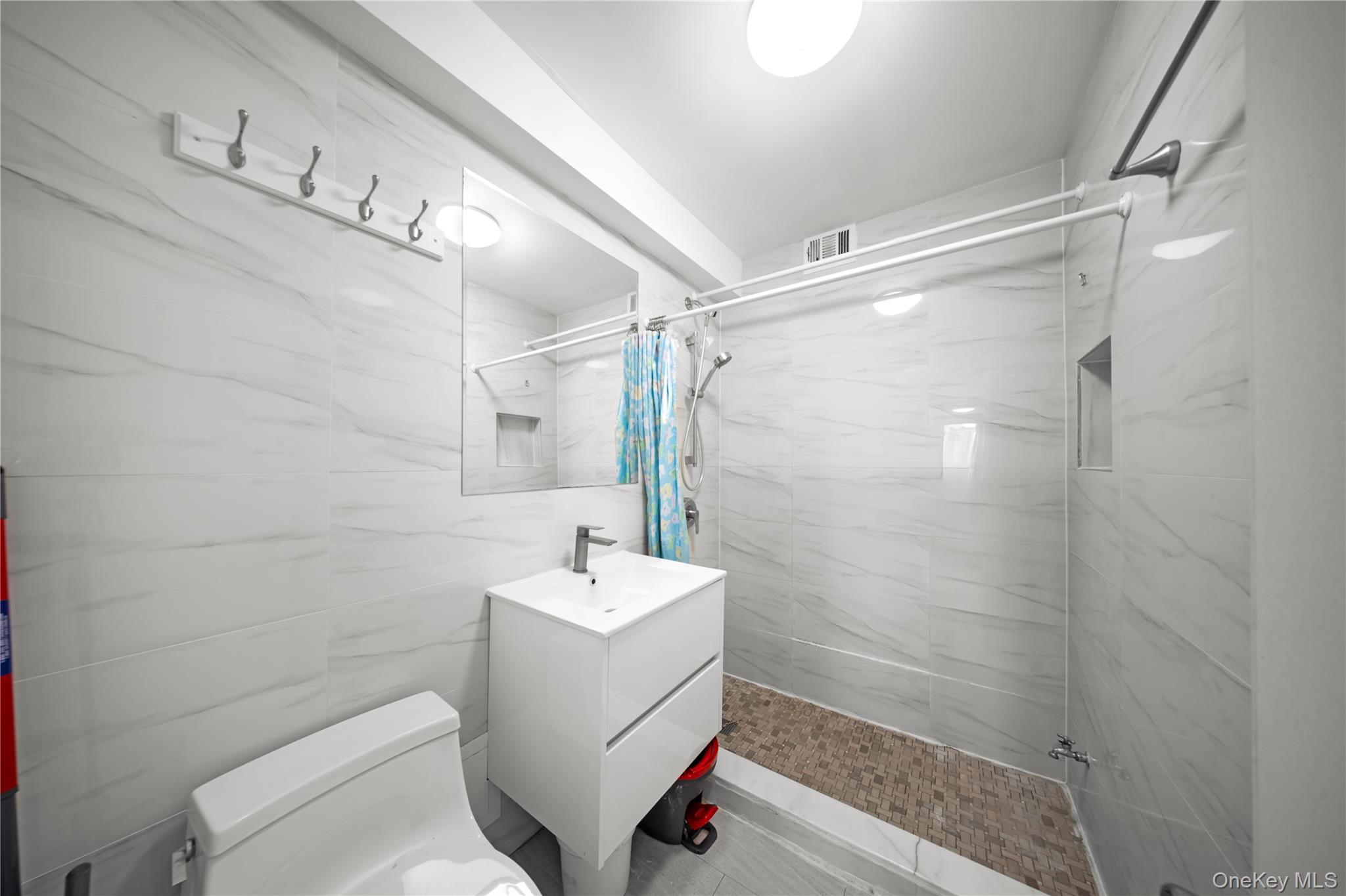 134-54 Maple Avenue, Unit 3W Queens, NY 11355 - Photo 16 of 19 Bathroom with vanity, a marble finish shower, and tile walls