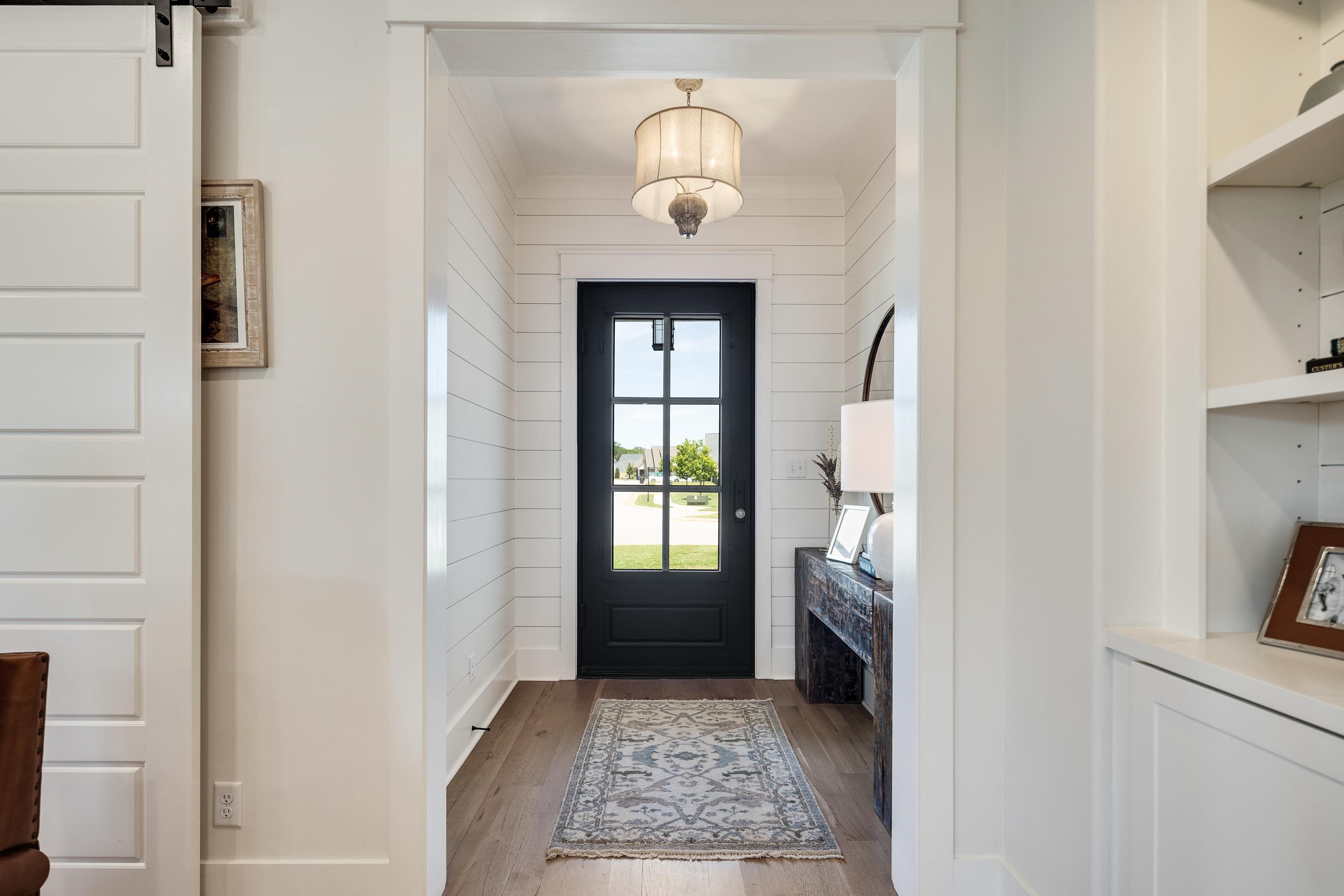 100 Sunflower View Road Piperton, TN 38017 - Photo 4 of 29 Entryway featuring a black paneled door with glass inserts, shiplap wall accents, wood-finish flooring, and a decorative pendant light fixture