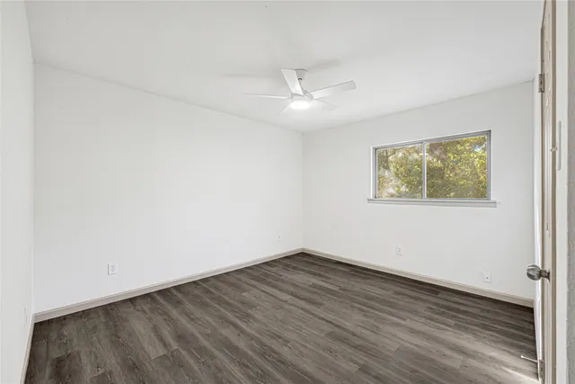 an empty room with wooden floor ceiling fan and windows
