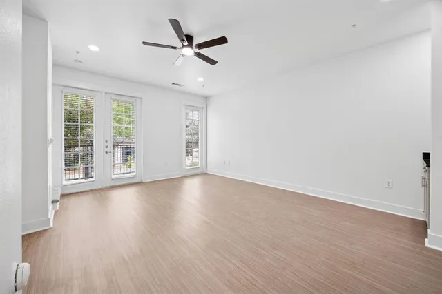 an empty room with wooden floor fan and windows