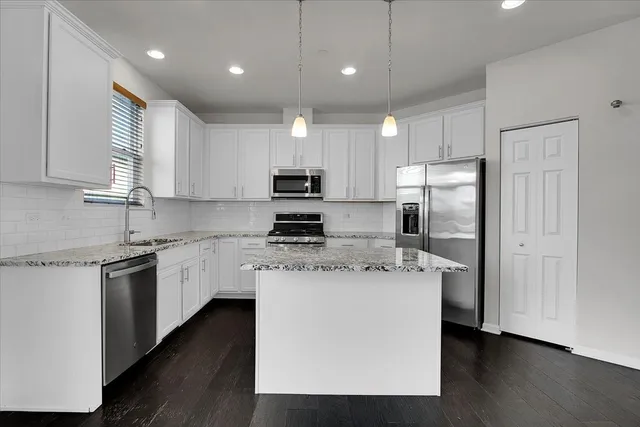 a kitchen with stainless steel appliances granite countertop a refrigerator a sink dishwasher a stove and white cabinets with wooden floor