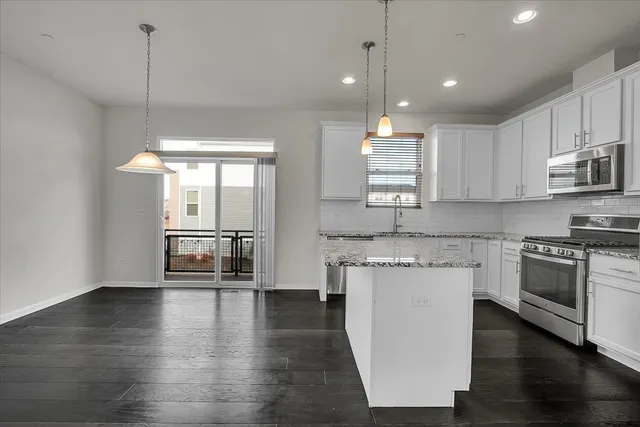 a kitchen with stainless steel appliances granite countertop a stove a sink and white cabinets with wooden floors