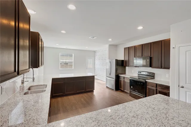 a kitchen with stainless steel appliances granite countertop a stove a sink a refrigerator and a granite counter tops with white cabinets