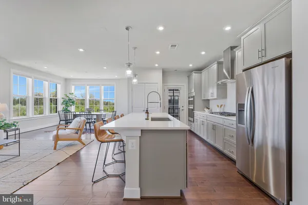 a kitchen with stainless steel appliances granite countertop a refrigerator a sink dishwasher a stove and a dining table with wooden floor