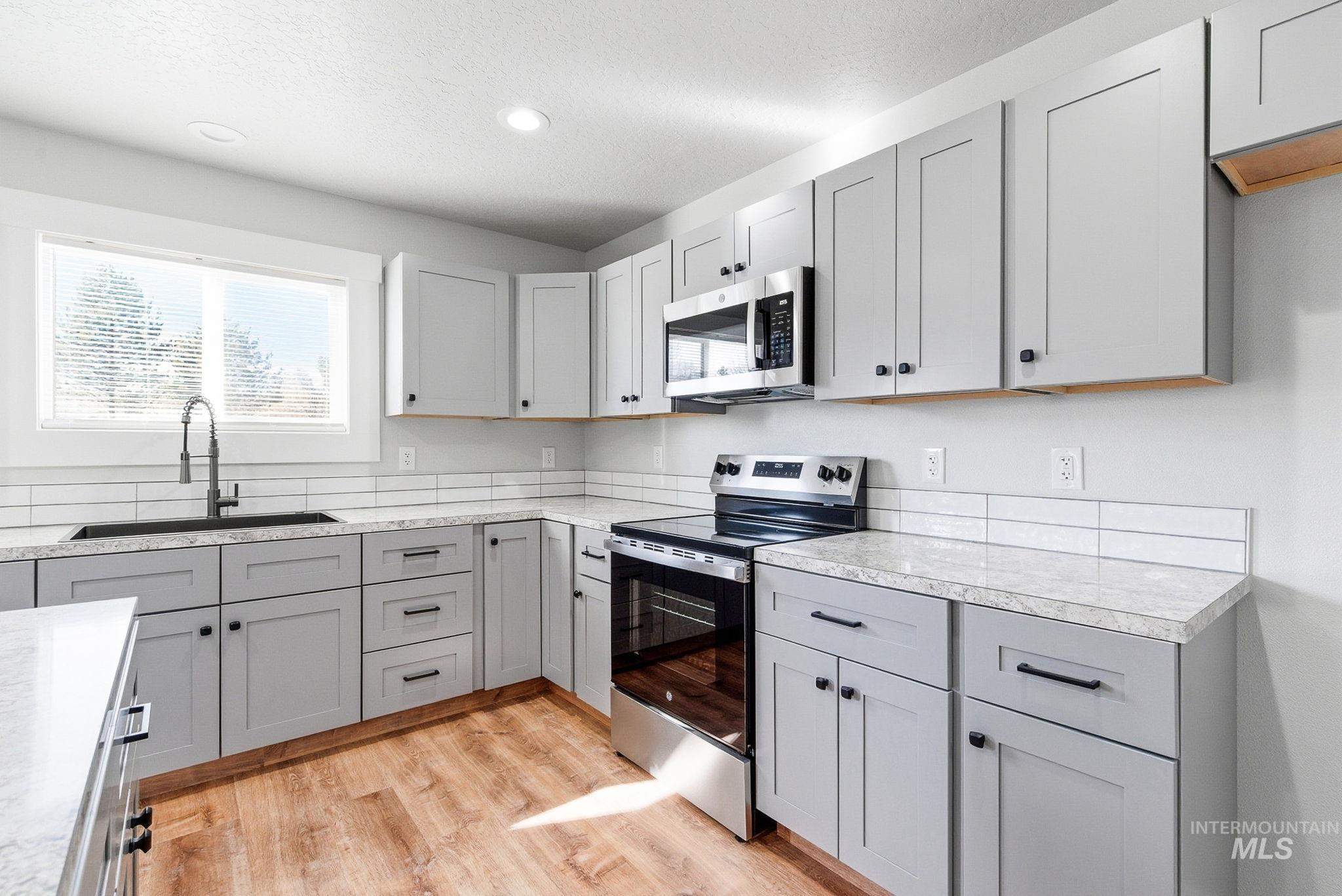 3312 Vistapark Drive Caldwell, ID 83605 - Photo 4 of 17 Kitchen with gray cabinetry, stainless steel appliances, light wood finished floors, healthy amount of natural light, and a textured ceiling