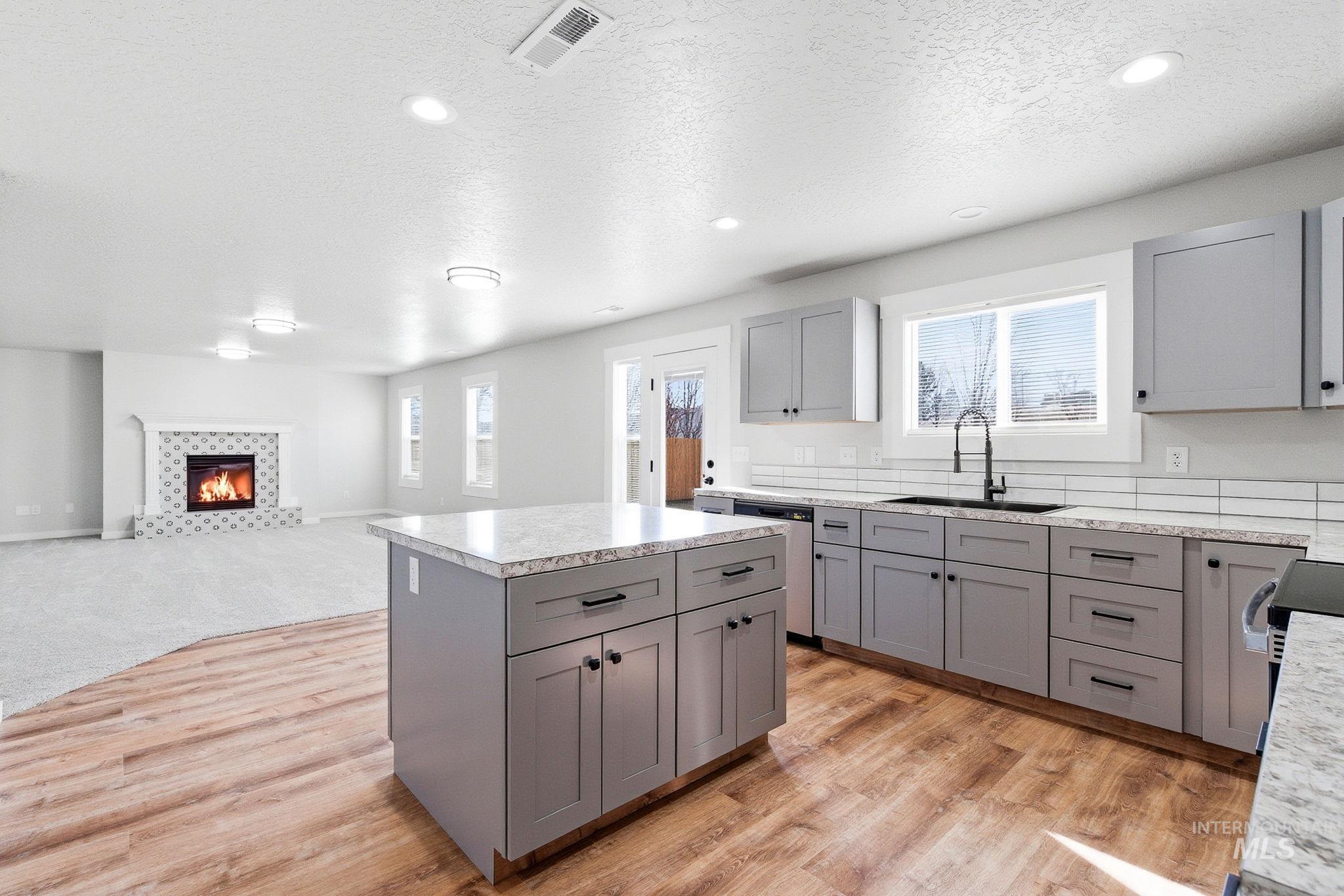 3312 Vistapark Drive Caldwell, ID 83605 - Photo 5 of 17 Kitchen featuring gray cabinets, light countertops, a kitchen island, a tiled fireplace, and a textured ceiling