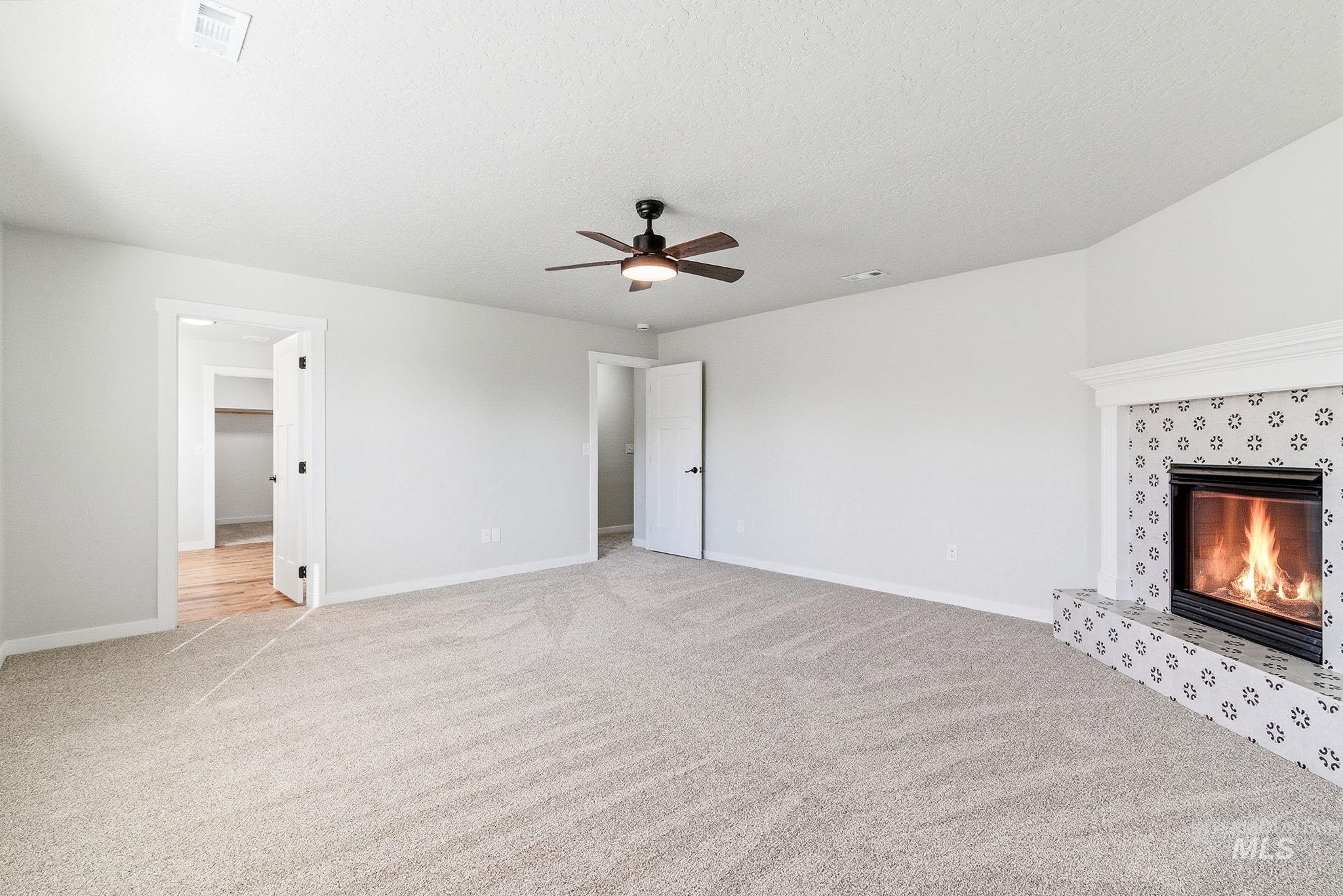 3312 Vistapark Drive Caldwell, ID 83605 - Photo 10 of 17 Unfurnished living room featuring light colored carpet, a tiled fireplace, ceiling fan, and a textured ceiling